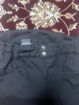 Svarta täckbyxor Polarn O. Pyret 146 - Svarta täckbyxor från Polarn O. Pyret i storlek 146. Byxorna har elastisk midja, dubbla knappar, reflexdetaljer på benen och är fodrade för extra värme. Perfekta för kalla dagar och vinteraktiviteter.