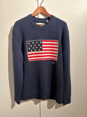 Mörkblå stickad tröja från Gant - Snygg mörkblå stickad tröja från Gant med amerikansk flagga i rött, vitt och blått framtill. Aldrig använt faktiskt! För stor för mig, insåg det efter att jag hade fått hem den. Kvitto finns! Möts helst upp!