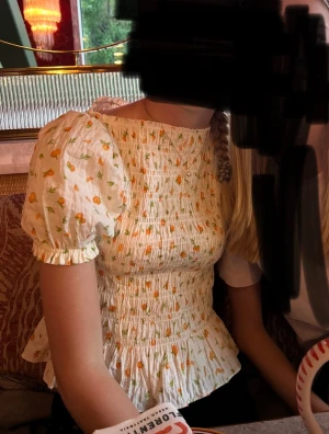 Vit blus med apelsiner och puffärmar - Säljer en söt vit blus med små apelsiner och gröna blad. Blusen har puffiga korta ärmar, smockad midja och volang nedtill. Perfekt för dig som gillar romantisk och trendig stil med fina detaljer. Den är från H&M och är i storlek S💗