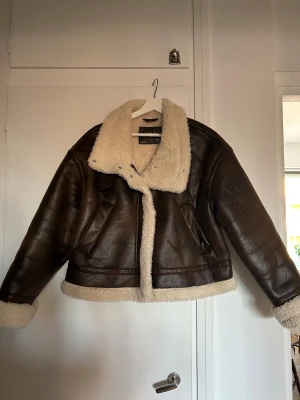 Brun teddyjacka med krage från Amisu  - Säljer en brun teddyjacka från Amisu med fluffig, krämvit fuskpäls på krage, insida och muddar. Jackan har en loose passform, två fickor och dragkedja framtill. Perfekt för dig som vill ha en cool och mysig look under höst och vinter.