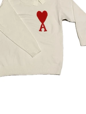 Vit stickad tröja  - Passar även M !Säljer en vit stickad tröja  med rött hjärta och bokstaven A broderat på bröstet. Tröjan har rund hals, långa ärmar och ribbade muddar vid ärmslut och nederkant. Perfekt för dig som gillar stilrena detaljer och snygg design. 
