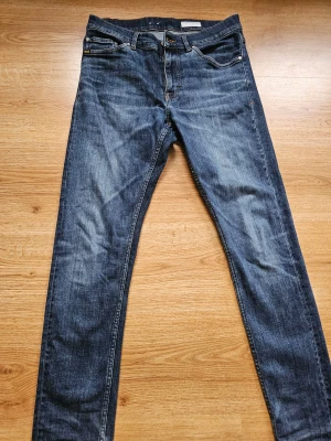 Tiger of Sweden blå jeans  - Snygga blå jeans från Tiger of Sweden med skinny fit och klassisk femficksdesign. Jeansen har en mörk tvätt med lätt slitning och bruna kontrastsömmar. Skinnpatch med logga bak i midjan. Perfekta för dig som gillar smalare siluett.