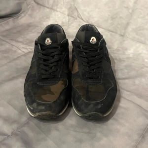 Moncler trainers - Tja! Vi säljer ett par snygga Moncler trainers med svart mocka och kamouflagemönster i gröna och bruna. Skorna är i hyggligt skick! Vid frågor och funderingar hör av er!😁