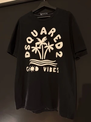 Svart Dsquared2 t-shirt - Svart t-shirt från Dsquared2 med stort vitt tryck framtill med palmer och texten 'Good Vibes'. Klassisk rund hals och korta ärmar. Tillverkad i 100% bomull för en skön och avslappnad känsla. Storlek L, knappast använd så är som ny! Köpt på Best secret så den är äkta!