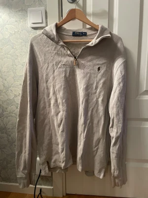 Beige half zip tröja Polo Ralph Lauren - Snygg beige långärmad tröja från Polo Ralph Lauren med half zip och klassisk krage. Tröjan har det ikoniska broderade logot på bröstet och är gjord i mjuk bomull. Perfekt för chill dagar och enkel att matcha med jeans eller chinos.