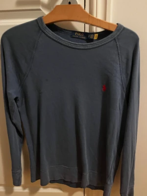 Blå långärmad tröja från Polo Ralph Lauren - Snygg mörkblå långärmad tröja från Polo Ralph Lauren med klassisk röd broderad logga på bröstet. Tröjan har rund hals och är gjord i mjuk bomull, perfekt för chill dagar. Enkel och stilren design som funkar till jeans eller shorts.