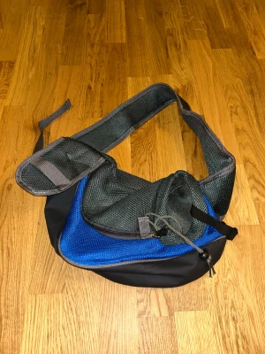 Svart och blå axelväska med meshdetaljer - Cool axelväska i svart och blått med bred, vadderad axelrem och meshdetaljer. Väskan har dragkedja och praktiska fack, perfekt för att bära med sig det viktigaste. Sportig look och smidig att ha över axeln.