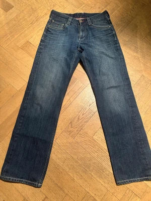 Tommy Hilfiger raka blå jeans - Klassiska blå jeans från Tommy Hilfiger med raka ben och normal passform. Jeansen har fem fickor, tydliga kontrastsömmar och diskret logga på myntfickan. Tillverkade i slitstarkt denim med snygg tvättad look och dragkedjegylf.