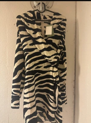 Zebramönstrad omlottklänning H&M - Snygg kort omlottklänning från H&M med zebramönster i svart och vitt. Klänningen har långa ärmar och en cool omlottdetalj framtill. Materialet känns lätt och skönt mot huden, perfekt för dig som gillar att sticka ut med djurmönster.