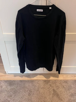Mörkblå  långärmad tröja Jack & Jones - En stilren svart långärmad tröja från Jack & Jones. Tröjan har en klassisk rund hals och är gjord i mjuk bomull, perfekt för dig som gillar enkel och clean stil. Passformen är normal och funkar till många olika outfits.