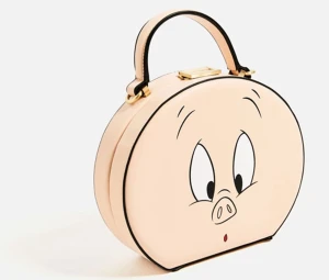 ZARA x Looney Tunes Porky Pig Minaudière - Superunik rund limited edition axelväska från ZARA x Looney Tunes Porky Pig Minaudière med ett gulligt grisansikte på framsidan. Väskan är ljusbeige/rosa med svarta detaljer och har både handtag och avtagbar axelrem i skinn.                                                               Width: ~6 in (15 cm) Height: ~7 in (18 cm) Length/Depth: ~9 in (23 cm)