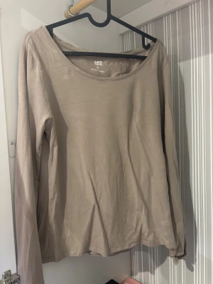 Beige långärmad topp från 157 - En enkel och stilren beige långärmad topp från 157. Modellen har rund halsringning och är tillverkad i mjuk bomull som känns skön mot huden. Perfekt att matcha med jeans eller kjol för en chill look.