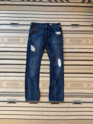 Jack and Jones jeans med slitningar - Snygga jeans grå Jack and Jones, de är använda o har unika slitningar men inga hål.  Oklart vilken storlek men här är måtten:  Innerben: 85 cm Midja: 42 cm Benöppning: 20 cm