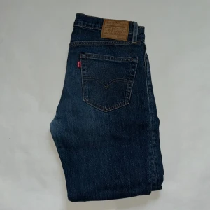 Levi's 511 mörkblå jeans W32 L30 - Snygga Levi's 511 jeans i mörkblå tvätt med klassisk femficksdesign och diskreta slitningar. Modellen har en slim passform och raka ben, med läderpatch bak i midjan och ikonisk röd Levi's-tag på bakfickan. Perfekta för en cool och avslappnad stil. Jag säljer dom eftersom att dom var lite små till mig. 