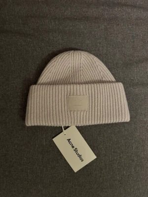 Vit/beige  stickad mössa Acne Studios - Snygg beige mössa från Acne Studios med ribbstickad design och uppvikt kant. 100% Ull. Butikpris: 1599 kr