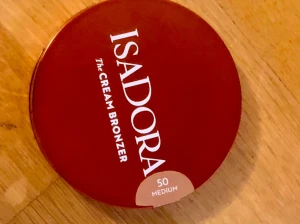 Isadora The Cream Bronzer 50 Medium - Säljer en Isadora The Cream Bronzer i nyansen 50 Medium. Kommer i en rund, rödbrun dosa med vit text. Perfekt för att ge ansiktet en naturlig solkysst look med krämig formula som är lätt att blenda.