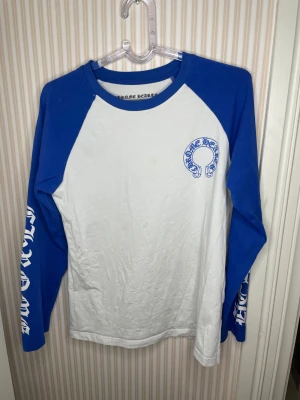Chrome Hearts långärmad t-shirt blå/vit - Långärmad t-shirt från Chrome Hearts med blå ärmar och vit kropp. Stora tryck på ärmarna och ryggen samt logga på bröstet. Skön bomullskvalitet och klassisk crewneck. Perfekt för dig som gillar streetwear och vill sticka ut.