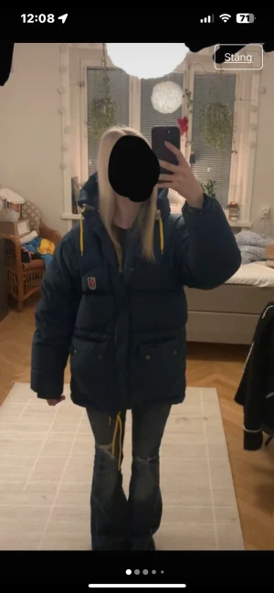 Mörkblå pufferjacka från Fjällräven - Säljer en mörkblå pufferjacka från Fjällräven i storlek XXXS. Jackan har gul snörning vid huvan, stora fickor med knappar och en rejäl dragkedja. Perfekt för dig som gillar oversized look och vill ha något varmt och stilrent med ikonisk Fjällräven-logga.