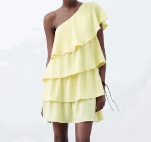 Zara klänning - Säljer en ljusgul kortklänning med flera volanger och snygg oneshoulder-design. Klänningen har en luftig och flowy passform, perfekt för sommarens alla tillfällen. Den är ärmlös på ena sidan och har en mjuk, feminin look. Säljer denna klänning från Zara i storlek M, super fin! Fint skick!