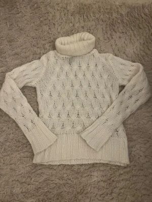 Vit stickad polotröja med mönster - Säljer en vit stickad polotröja i storlek 34 med snyggt hålmönster och breda ribbade muddar vid ärmslut och nederkant.  Super söt och snygg!