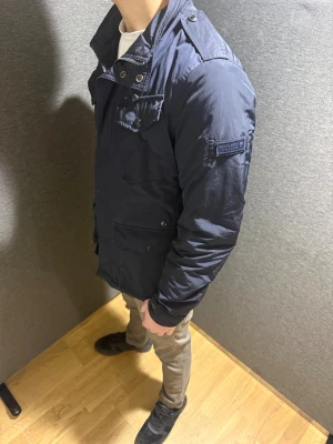 Mörkblå feeld jacka från Woolrich - Feeld jacket från Woolrich i mörkblå färg med flera praktiska fickor och detaljer som axelklaffar och dragkedja. Materialet är slitstark, perfekt för kyliga dagar. Modellen är 176 cm lång och väger 70 kg, jackan är stor för att vara XS, så sitter mer som S. Nypris på jackan är runt 5000kr, och väldigt svårt att hitta. Hör gärna av er vid minsta fråga eller mer information. (Priset går att diskutera)👍