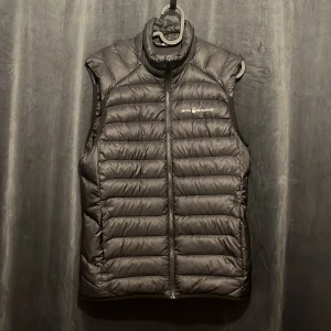 Svart dunväst från Sail Racing - Svart dunväst från Sail Racing med quiltad design och hög krage. Västen har dragkedja framtill och diskret logga på bröstet. Materialet är lätt och isolerande, perfekt för lager-på-lager. Snygg och sportig look som funkar till många stilar. Slimfit, storlek small och den är lite liten i storleken. Finns även två innerfickor.