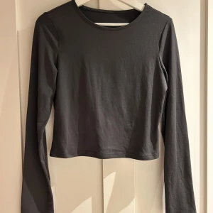 Grå långärmad topp  - En stilren grå långärmad topp, tillverkad av mjuk och stretchig polyester med lite elastan för extra komfort. Enkel design med rund hals och slät yta, perfekt att matcha med jeans eller kjol för en clean look.