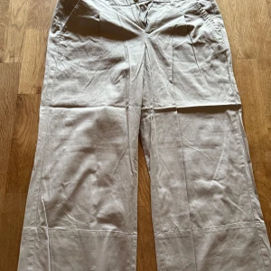 Beiga wide byxor från KappAhl - Snygga beiga byxor från KappAhl i storlek 42. Modellen är wide med raka ben och har fickor både fram och bak med knappdetaljer. Tillverkade i mjukt bomullsmaterial som känns skönt mot huden. Perfekta för en chill och stilren look.            lite skrynkliga då de varit nerpackade i vakum-påse. Något stretchiga. 