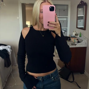 Svart ribbad topp med öppna axlar - Säljer en svart ribbad topp med lång ärmar. Helt nytt skick!! 