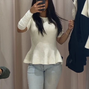 Söt topp/t-shirt men vågigt  - Supersöt vit stickad topp med ribbad struktur och peplumformad nederkant. Rund halsringning och korta ärmar ger en fräsch vibe. Perfekt att styla med jeans eller kjol för en clean look.