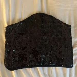 Svart paljettkorsett med snörning - Säljer en svart korsett-topp med glittriga paljetter över hela ytan. Toppen har snörning baktill för justerbar passform och en snygg, strapless design. Perfekt för att sticka ut på festen med sin glansiga look och coola detaljer. Den perfekta toppen till nyår!