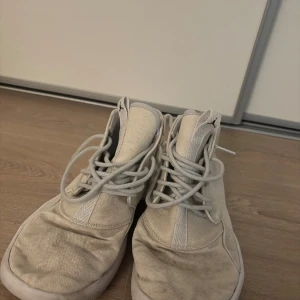 Vita Nike Air Jordan sneakers - Säljer ett par vita Nike Air Jordan sneakers med högt skaft och klassisk Jumpman-logga i svart på hälen. Skorna har snörning och är tillverkade i canvas med platt sula och rund tå. Perfekta för dig som gillar streetstyle och vill ha en clean look.