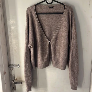 Beige kofta  - Mysig beige kofta från Lindex med djup v-ringning och en knapp framtill. Tröjan är croppad med ribbade muddar och har lång ärm. Perfekt för lager-på-lager och chill stil. Materialet är stickat och känns mjukt mot huden.