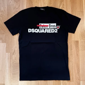 Svart DSQUARED2 t-shirt med tryck - Svart t-shirt från DSQUARED2 med stort vitt och rött tryck på bröstet där det står 'Catch Bros' och 'DSQUARED2'. Klassisk rund hals och korta ärmar. Snygg och stilren design som sticker ut med sitt grafiska tryck.