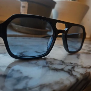 Svarta glasögon Corlin Sam 54-20 - Snygga svarta glasögon från Corlin i modellen Sam, storlek 54-20. Rektangulär form med markerad båge och cool detalj vid näsryggen. Passar dig som gillar en modern och stilren look. Tillverkade i blankt syntetmaterial.