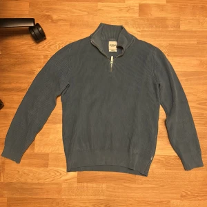 Blå ribbad half zip tröja Dobber - Snygg blå ribbad tröja från Dobber i storlek medium. Tröjan har en hög krage med half zip-dragkedja och är långärmad. Materialet är stickad bomull som känns mjukt och skönt mot huden. Perfekt för dig som gillar stilrena och bekväma plagg.