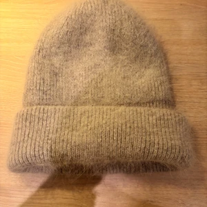 Grå fluffig mössa från Tête - Supermjuk och fluffig beige mössa från Tête. Klassisk ribbstickad modell med uppvikt kant och diskret luddig yta.