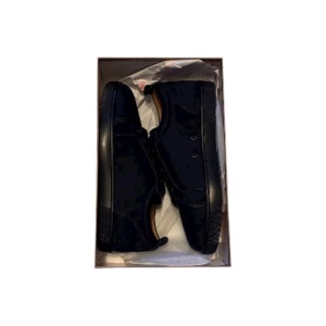 Christian Louboutin svarta sneakers - Snygga svarta sneakers från Christian Louboutin med klassisk röd sula. Skorna har rund tå, snörning och är tillverkade i mocka och skinn. Insidan är beige med guldfärgad logga. Perfekta för dig som vill ha en lyxig och stilren look.