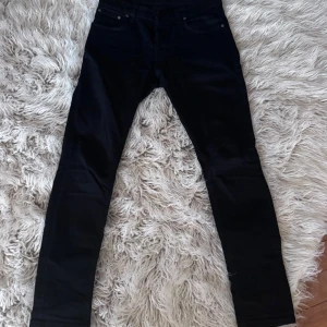 Svarta skinny jeans från Nudie Jeans - Svarta jeans från Nudie Jeans med skinny passform och klassisk femficksdesign. Jeansen har en smal siluett och är tillverkade i stretchigt denim för extra komfort. Perfekta för dig som gillar en tajt look och stilrena detaljer.