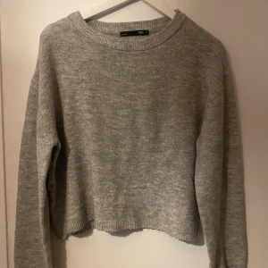 Grå stickad tröja från 157 - Mysig grå stickad tröja från 157 med rund hals och ribbade muddar. Modellen är lite loose och har långa ärmar, perfekt för att chilla eller hänga med vänner. Enkel och stilren design som funkar till jeans eller mjukisbyxor.