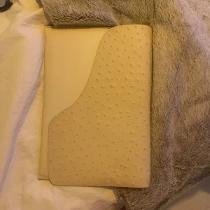 ATP atelier - Snygg beige kuvertväska från ATP Atelier i struts skin  med cool prickig struktur på locket. Stilren och minimalistisk design som passar perfekt till din laptop eller dokument. Väskan har en unik form och känns riktigt exklusiv.