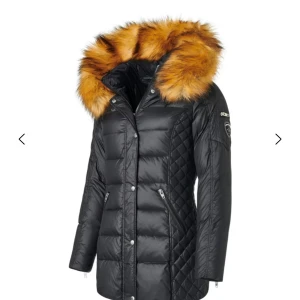 Svart dunjacka med päls från Rockandblue - Snygg svart dunjacka från Rockandblue med fluffig brun päls på huvan. Jackan har quiltade detaljer på sidorna, dragkedjor vid fickorna och en badge på ärmen. Perfekt för dig som vill ha en varm och stilren look under vintern.