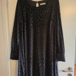 Svart klänning / tunika  - Cool svart klänning / tunika från Cellbes med glansigt mönster. Klänningen har långa ärmar med breda muddar och är tillverkad i mjuk polyester. Rund halsringning med knapp i nacken ger en snygg detalj. Perfekt för dig som gillar djurmönstrat och vill sticka ut. Nyskick, aldrig använd. 