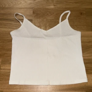 Vit ribbad linnetopp med smala band - Säljer en enkel och stilren vit ribbad linnetopp med smala axelband och v-ringad hals. Toppen är croppad och har en mjuk, stretchig känsla som gör den perfekt till varma dagar. Passar snyggt till både jeans och kjol.