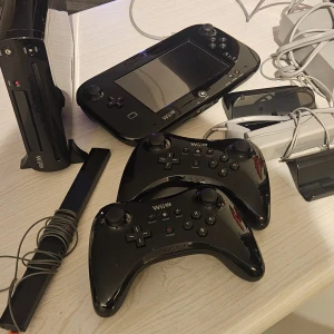 Nintendo Wii U + Wii Fit Plus Bundle - Komplett Nintendo Wii U med två Pro-kontroller, GamePad, sensorräls, Wii Fit Balance Board och flera populära spel som Wii Fit Plus, Wii Sports Resort och No More Heroes. Allt i gott skick, mindre slitage på tillbehör. Perfekt för familjespel och träning! Kan även säljer delar separat. Kom med bud...