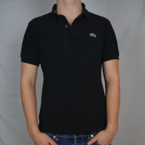 Lacoste Piké  - Snygg svart piké från Lacoste i storlek 3, motsvarar medium. Pikén är i gott skick och har inga defekter. Vid frågor eller funderingar är det bara att höra av sig, och kom ihåg, alltid 14 dagars ångerrätt hos oss på Revalo!