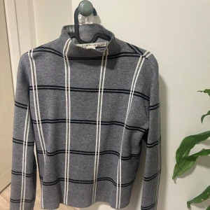 Grå polotröja med ränder från Max Studio - Snygg grå polotröja från Max Studio med vita och svarta ränder. Tröjan har hög krage och långa ärmar, perfekt för dig som gillar stilrena och klassiska mönster. Mjuk och skön kvalitet som passar till jeans eller kjol.