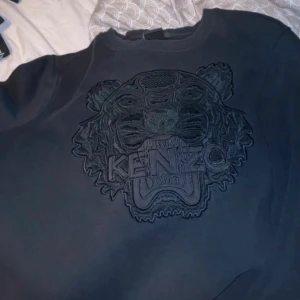Svart Kenzo sweatshirt med tigerbroderi - Svart sweatshirt från Kenzo med stort broderat tigerhuvud och logga på bröstet. Tröjan har rund hals och är långärmad, perfekt för dig som gillar statement-plagg och snygga detaljer.