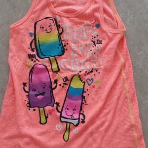 Topp - Säljer en orange/korall topp med färgglada glassar och texten 'BFFs are so chill!' framtill. Toppen har roliga tryck i blått, gult, lila och rosa samt små hjärtan. Perfekt för sommarens varma dagar.