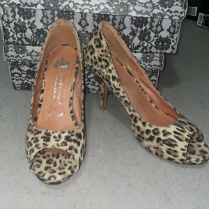 Leopardmönstrade pumps från Friis & Company - Snygga pumps från Friis & Company med leopardmönster i beige och svart. Skorna har öppen tå, hög klack och rundad form framtill. Utsidan är i ett mockaliknande material som ger en lyxig känsla. Perfekta för dig som vill sticka ut med ett djurmönstrat statement.